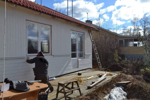 Byggare utför fasadarbete på ett litet hus med verktyg och material