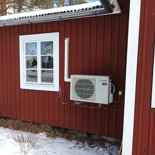 Utomhusdel av Mitsubishi luftvärmepump monterad på röd träfasad under fönster