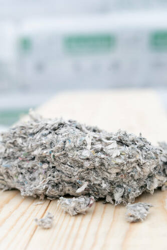 Närbild på lösullsisolering i cellulosa på träunderlag med ISOCELL-säckar i bakgrunden