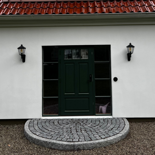 Bild på en dekorativ entré med cirkulär smågatstensläggning framför grön ytterdörr