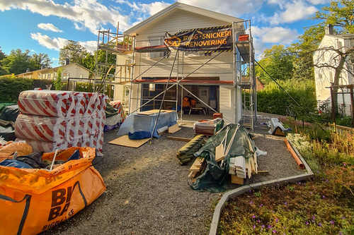 Pågående fasadrenovering av villa med byggställning, byggmaterial och banner