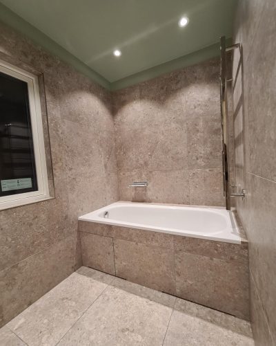 Badrumsrenovering Täby med infällt badkar, stenlook på väggar och grönt tak med spotlights