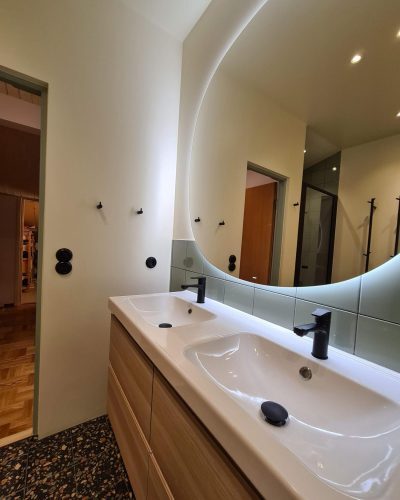 Badrum i Täby med dubbelhandfat, LED-belyst spegel och terrazzo-golv – modern design