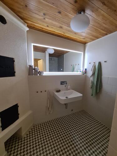 Badrum med LED-spegel, schackrutigt klinkergolv och träpanel i tak