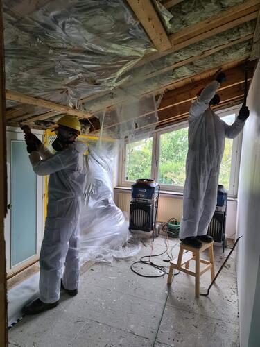 Två hantverkare i skyddskläder som arbetar med isolering i taket vid en renovering