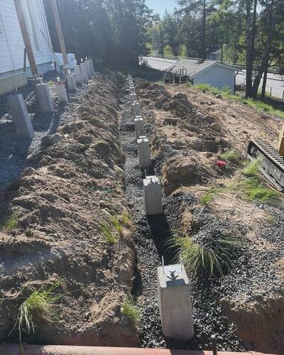 Grundarbete med betongplintar för altanbygge vid vit villa – plintgrundläggning i kuperad terräng
