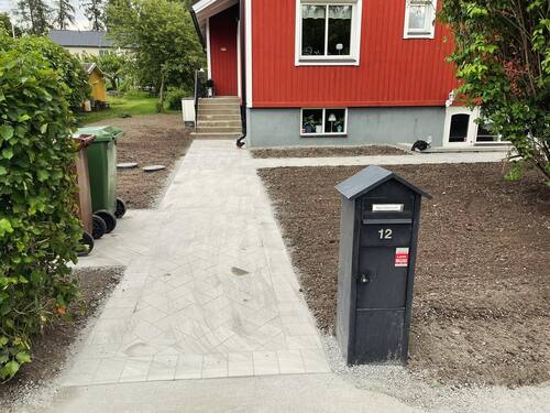Plattsättning och entrégång med postlåda vid röd villa – stenläggning och markplanering i Norrtälje