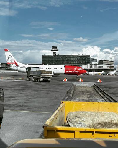 Transport och marklogistik på flygplats – tungt anläggningsarbete med vy över Norwegian-plan på Arlanda