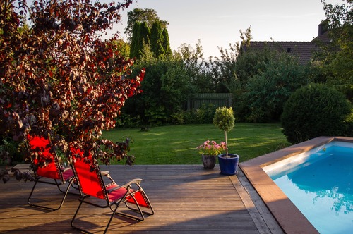 Trädäck och pool i trädgårdsmiljö med röda stolar