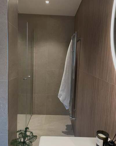 Modern duschlösning i Gävle med glasvägg och strukturkaklade väggar – del av badrumsprojekt utfört av LA Rörsystem AB i Sandviken.