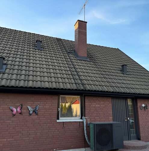 Färdiglagt svart tegeltak med skorsten och dekorationer på fasaden till tegelhus i kvällsljus.