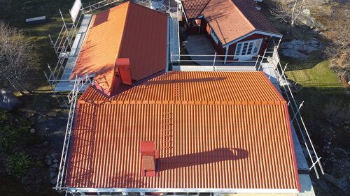 Ett rött hus med rött tak sett uppifrån, med byggställningar runt.