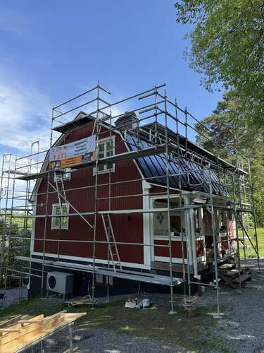 Ett rött hus med byggställningar runt fasaden under takarbete.