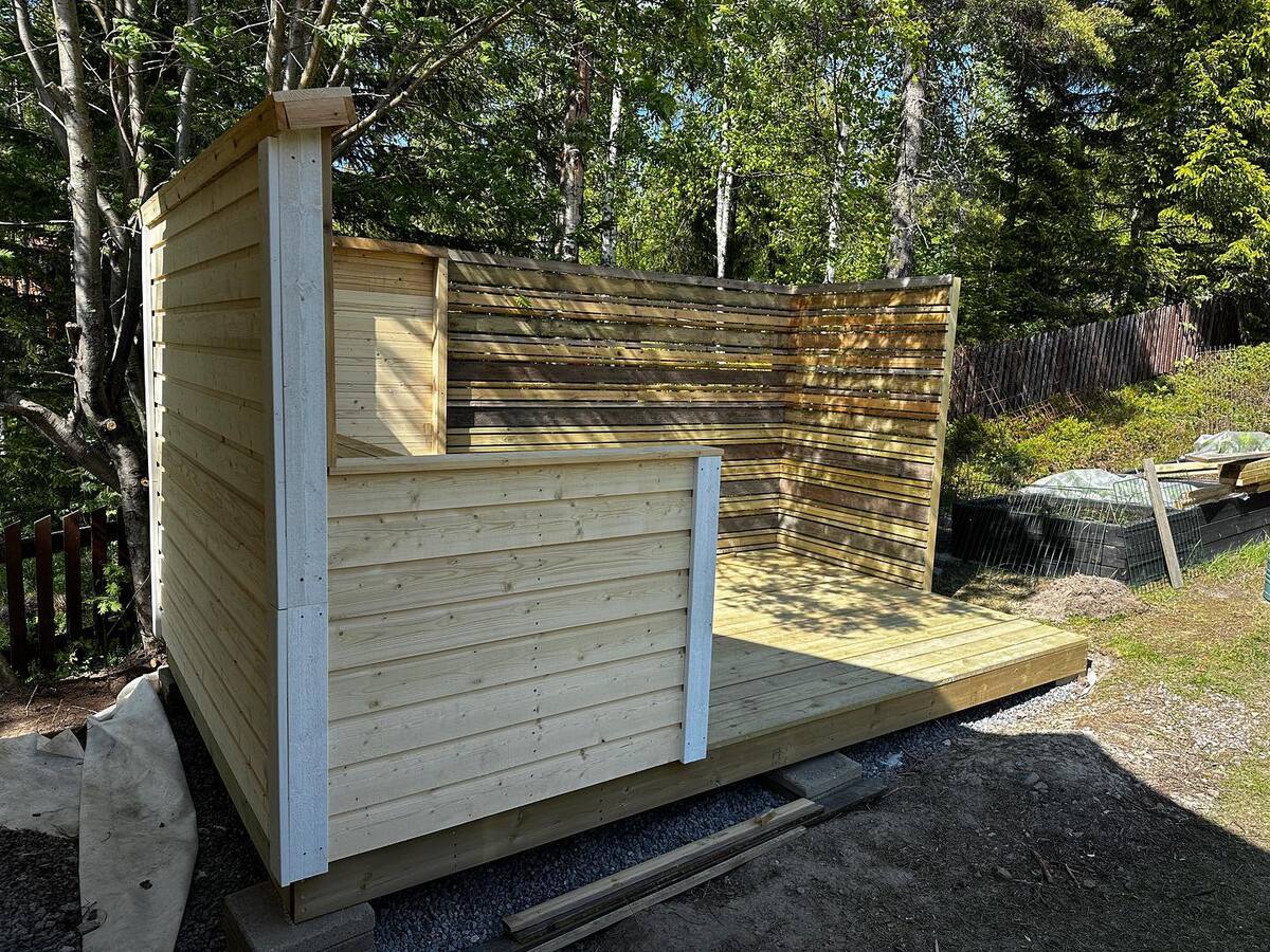 Träkonstruktion under uppbyggnad i trädgård, med väggar i stående panel och öppen fram- och taksida. Träkonstruktion under uppbyggnad i trädgård, med väggar i stående panel och öppen fram- och taksida.