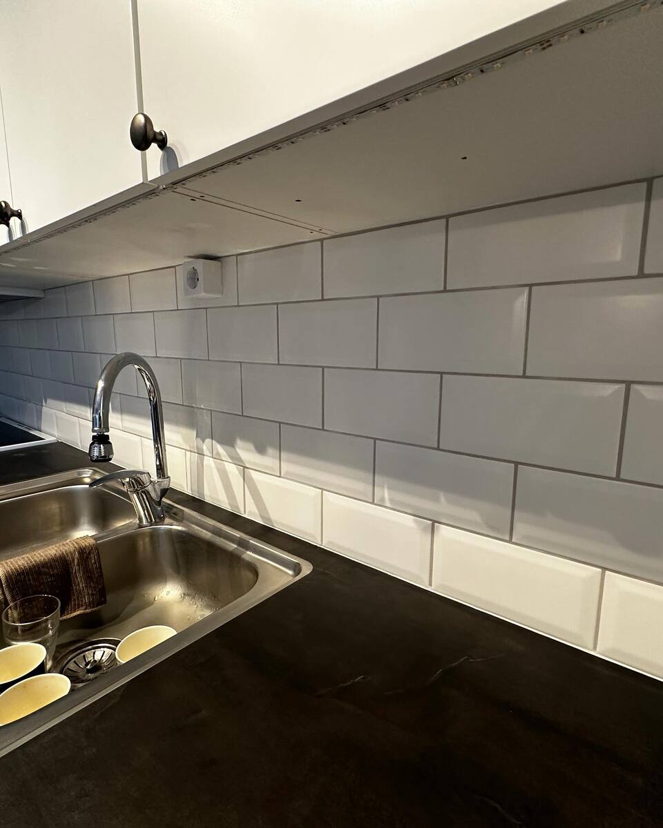 Närbild på diskbänk i rostfritt stål med vitt kakel ovanför och vita överskåp. Närbild på diskbänk i rostfritt stål med vitt kakel ovanför och vita överskåp.