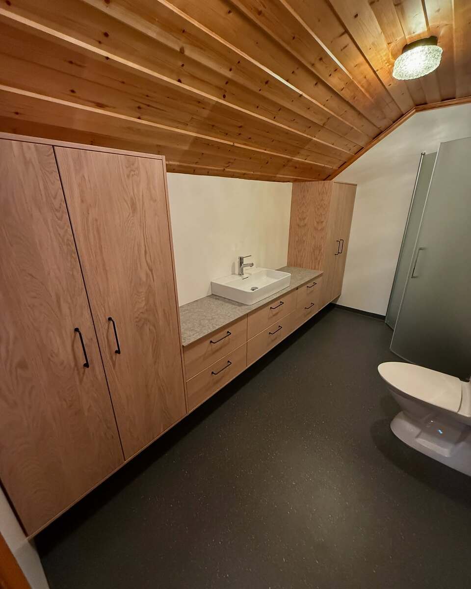 Badrum med snedtak och träpanel i taket, utrustat med träskåp, handfat och dusch med frostat glas. Badrum med snedtak och träpanel i taket, utrustat med träskåp, handfat och dusch med frostat glas.