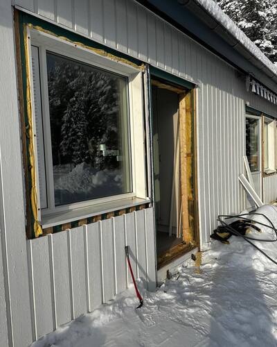 Fasad med nyligen installerade fönster under vintertid, med snö på marken och synlig isolering runt karmarna.