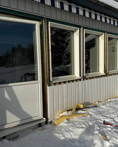 Pågående fönsterbyte på en grå villa under vintern, med isolering synlig runt fönstren