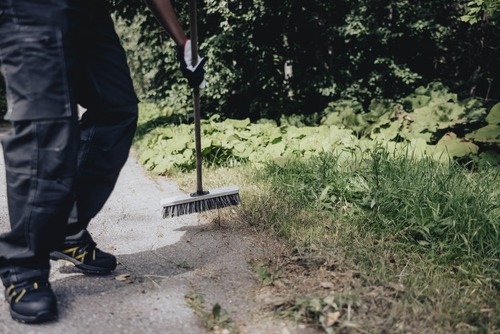 En person sopar bort gräs och löv från en gångväg med en borste.