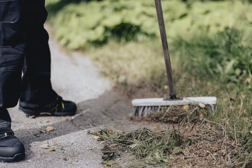 En sopborste används för att rensa en gångväg från löv och gräsrester.
