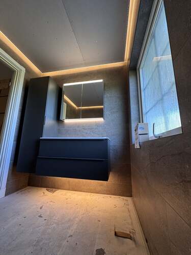 Badrum under renovering med installerad LED-belysning bakom spegel och överskåp.