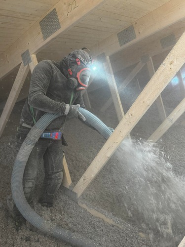 Installatör som blåser lösullsisolering på vind mellan takbjälkar