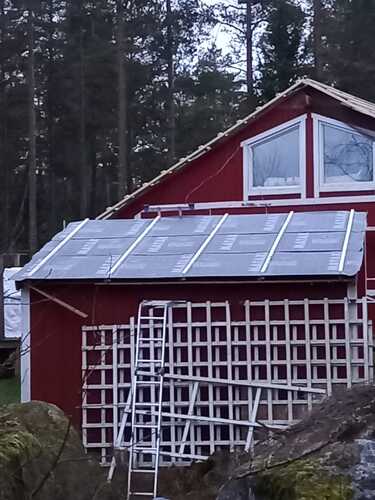 Rött hus med tak under renovering i skogsområde