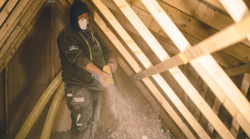 Arbetare som blåser lösullsisolering i snedtak på vind