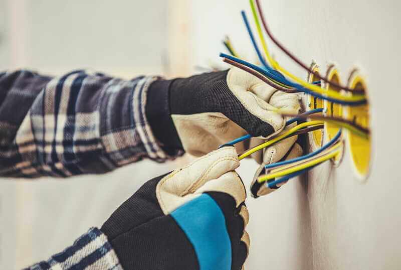 Elektriker med handskar kopplar elkablar i vägg