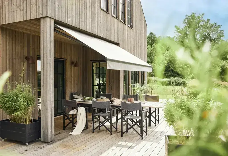 Utfälld terrassmarkis i ljust tyg över träterrass med utemöbler