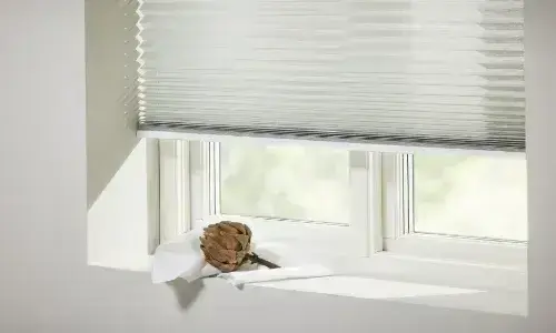 Vit plisségardin nedfälld över fönster med infallande dagsljus
