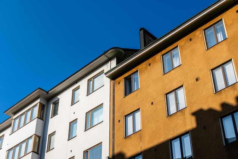 Putsade fasader i vitt och gult på flerbostadshus mot blå himmel
