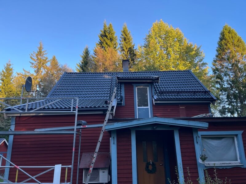 Rött hus med mörkt tak och ställning uppsatt vid takarbete