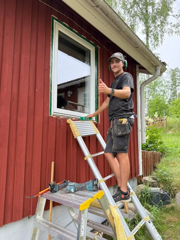 Montör som installerar nytt fönster på rödmålad husfasad