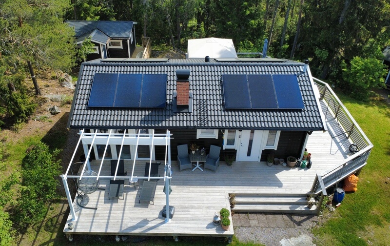 Flygbild över hus med svart tegeltak, solpaneler och uteplats