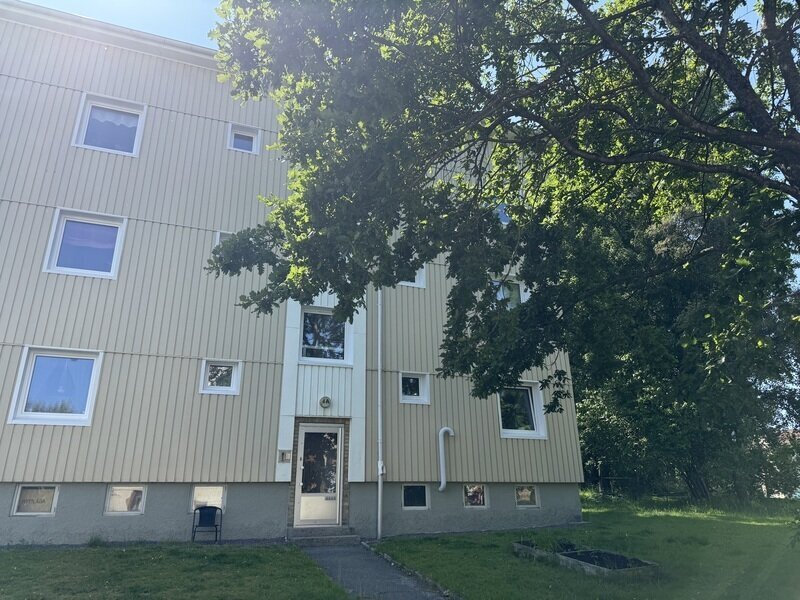 Flerbostadshus med ny träpanelfasad och vita fönster sett från entrésidan
