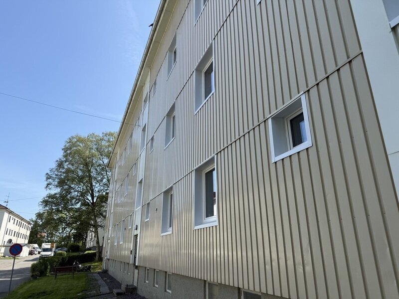 Närbild på vertikal träpanelfasad med nyinstallerade vita fönster underifrån