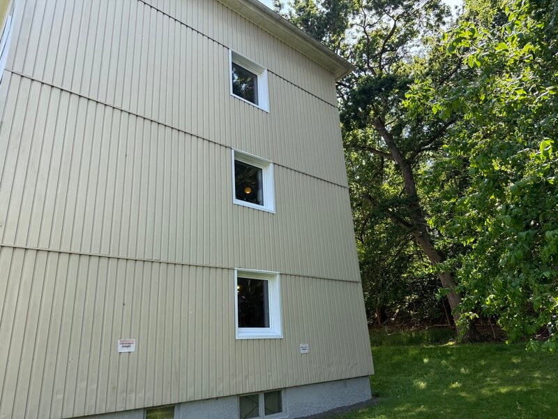 Gavel på flerbostadshus med nyinstallerade vita fönster omgivet av lövträd