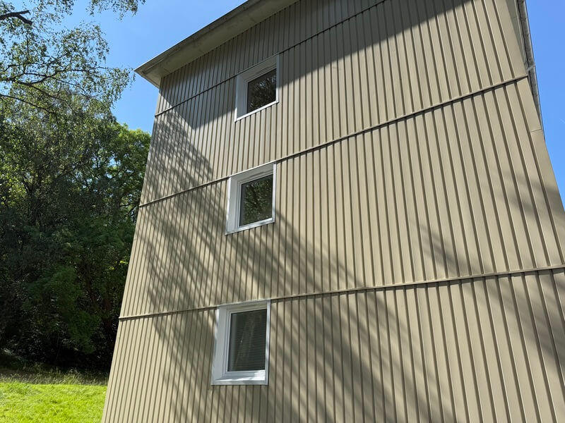 Gavel på flerbostadshus med nyinstallerade vita fönster i ljus vertikal träpanel