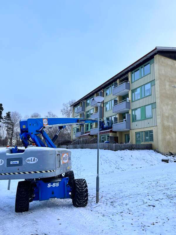 Skylift uppställd vid flerbostadshus under pågående fönsterbyte i vinterväglag