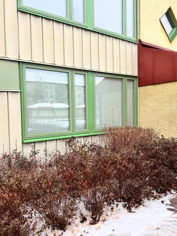 Närbild på nyinstallerade fönster med gröna karmar och persienner på putsad fasad