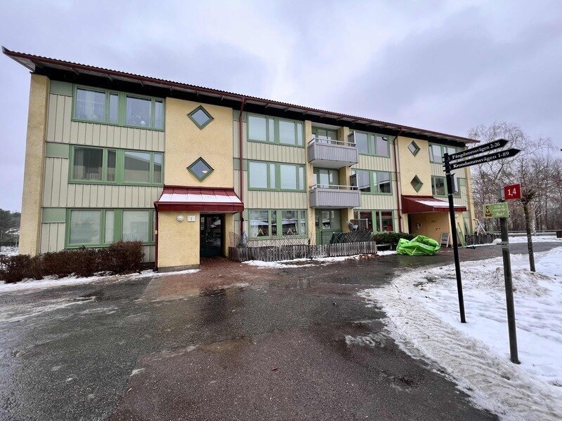 Flerbostadshus med gröna fönsterprofiler och röda plåtdetaljer i vinterväglag