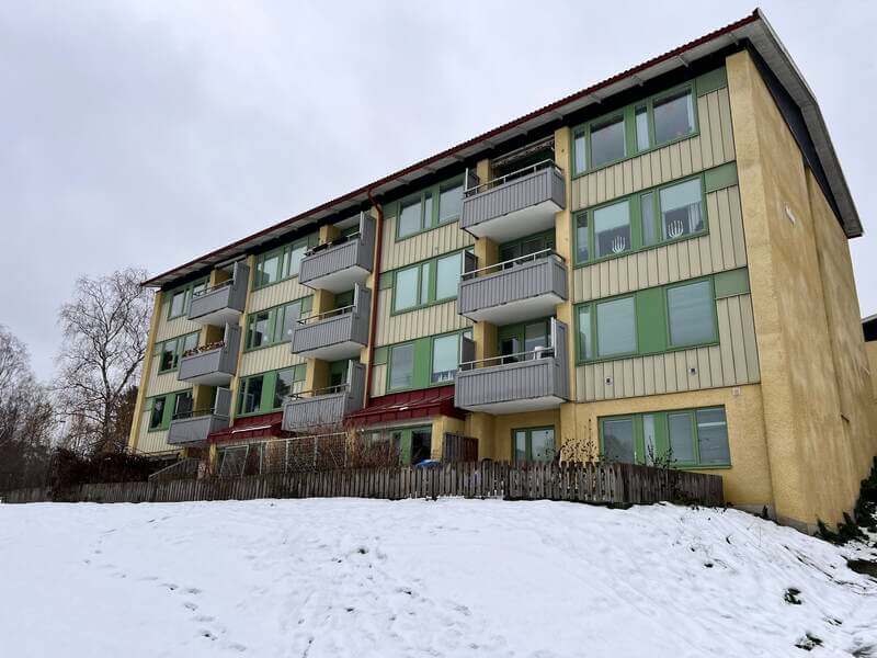 Flerbostadshus med gröna fönsterprofiler och balkonger sett från snötäckt trädgård
