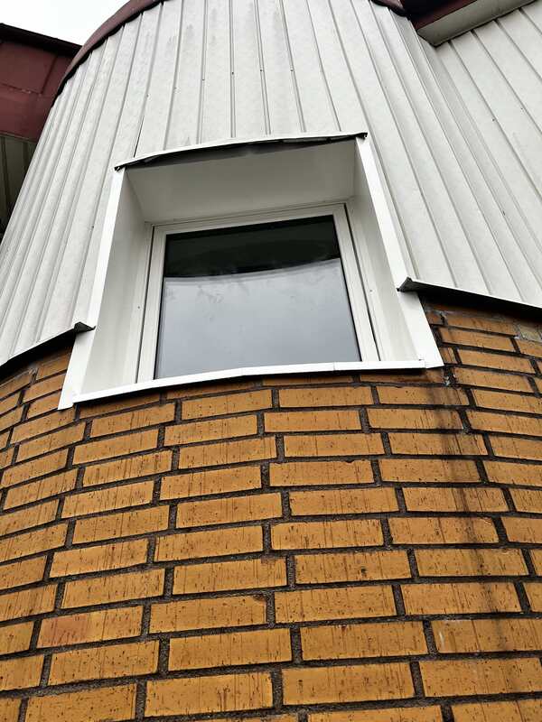 Närbild på nyinstallerat fönster med vit plåtinklädnad på rund tegelfasad