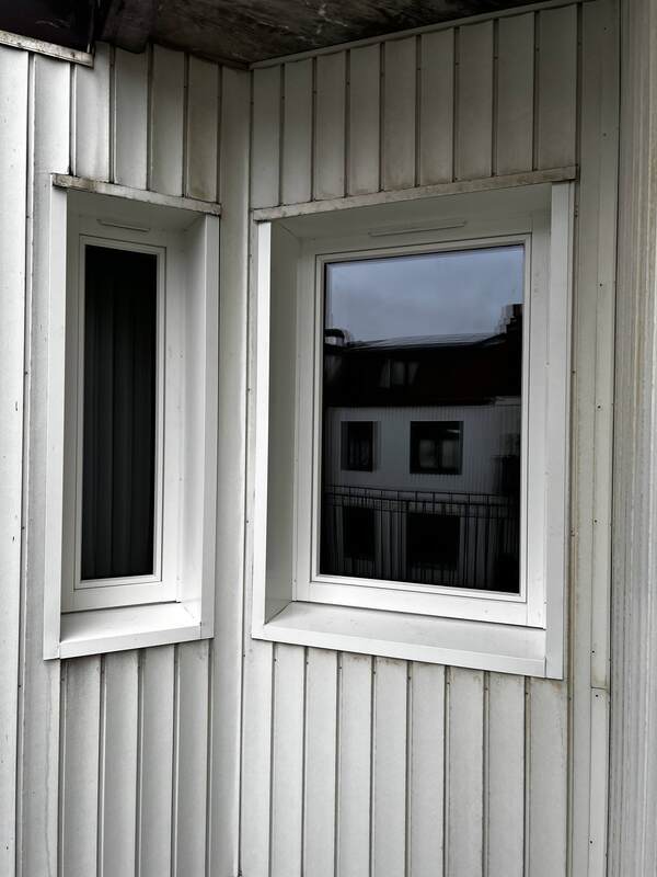 Nyinstallerade höga fönster med vita karmar och foder på vit träpanelfasad