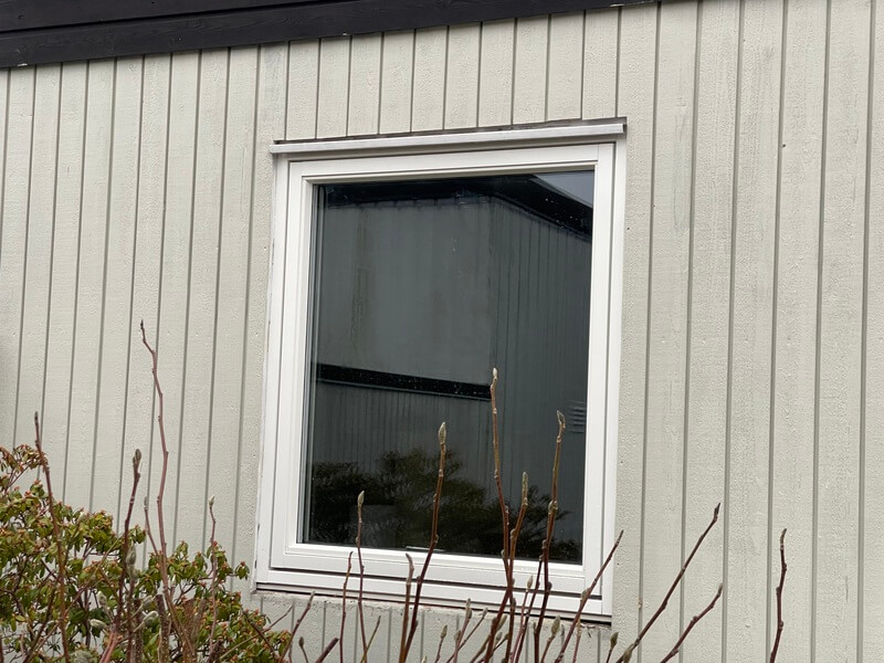 Nyinstallerat fönster med vit karm och underbleck på grå vertikal träpanelfasad