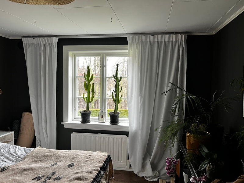 Närbild på nyinstallerat fönster med vit karm och fönsterbänk med kaktusar i mörkt rum