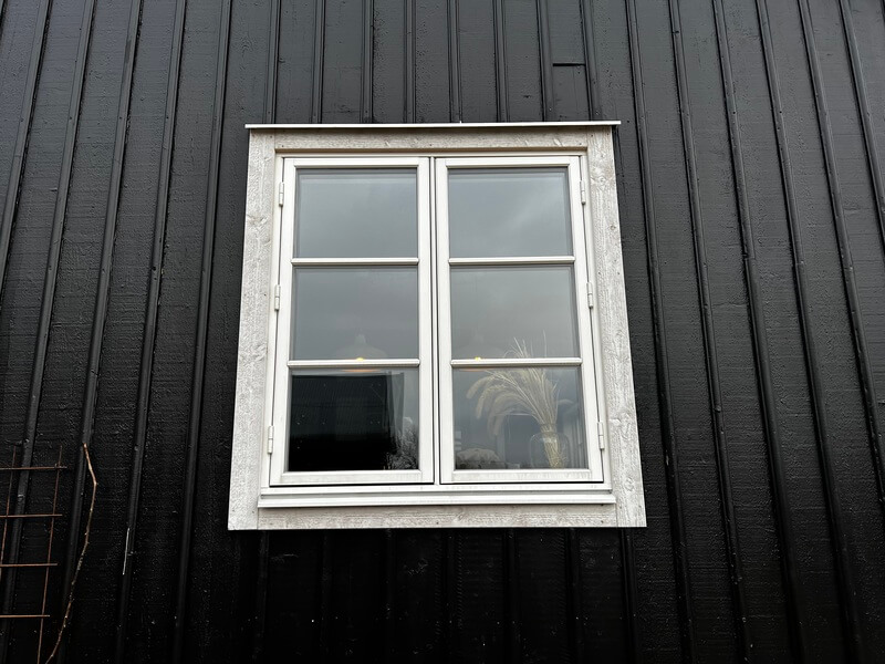 Närbild på nyinstallerat tvåluftsfönster med vit karm på svart träpanelfasad