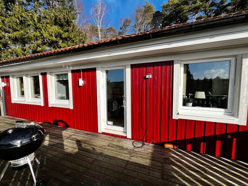Röd träpanelvilla med nyinstallerade vita fönster mot trädäck i solsken