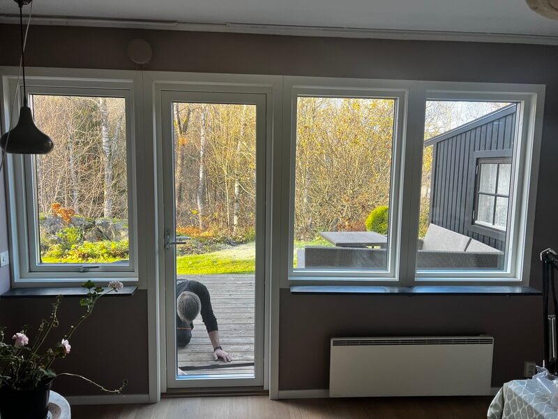 Tre nyinstallerade fönster med vita karmar i rad med utsikt mot trädgård och altan